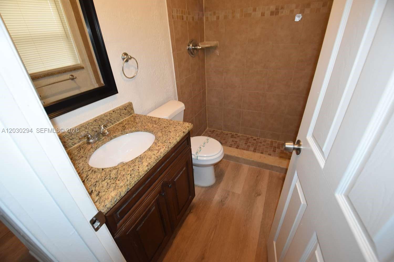 A bathroom features a granite vanity, a toilet, and a tiled walk-in shower — SUNRISE, FL
