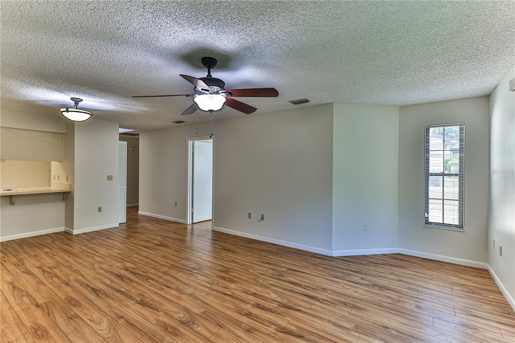 An open-concept living area features wood-look flooring, a ceiling fan, and a pass-through kitchen window — 3333 S LIVERPOOL POINT, INVERNESS, FL