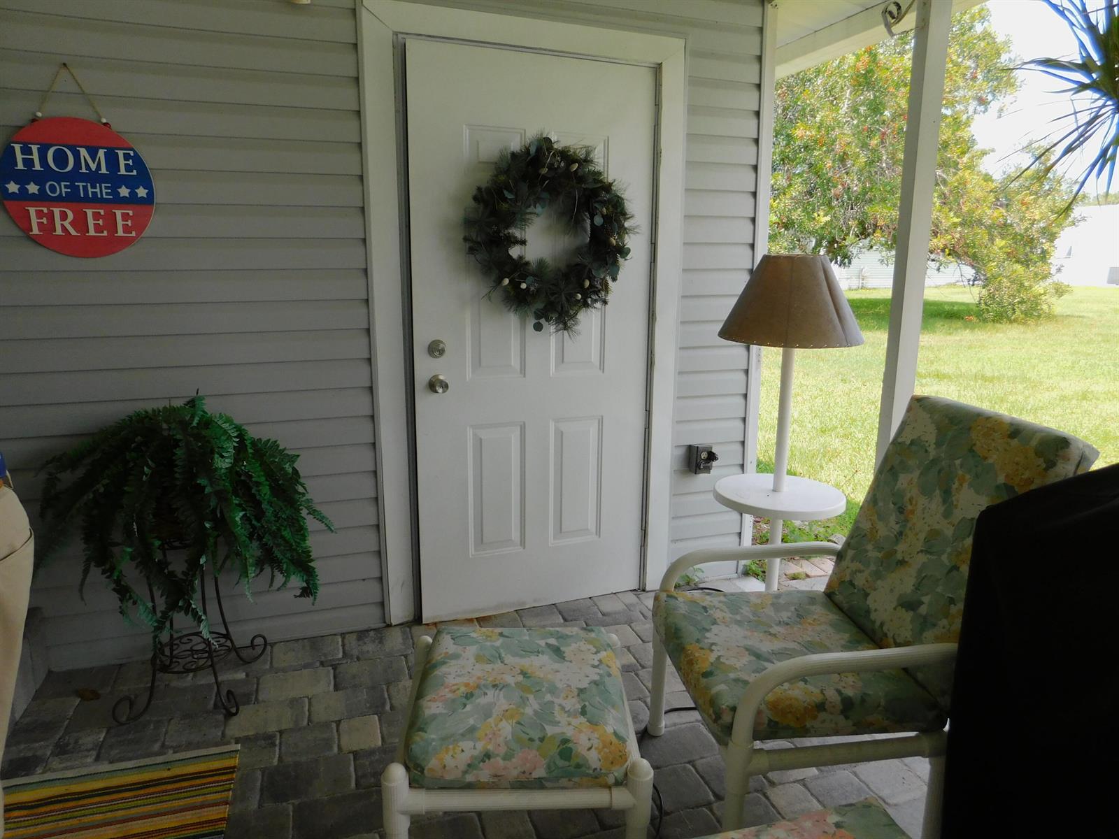 A covered porch features a white door with a wreath, floral furniture, and a lamp — 485 Hemingway Terrace # 04, Fort Pierce FL 34982, FORT PIERCE, FL