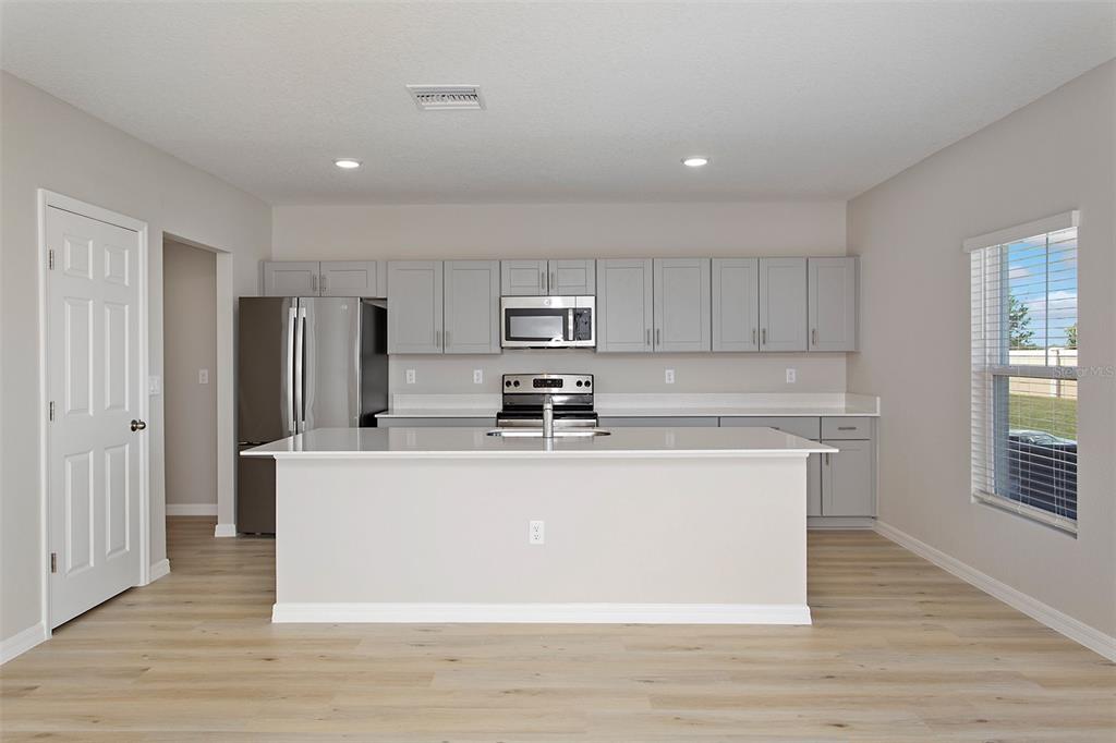 A modern kitchen features light gray cabinets, stainless steel appliances, and a large white island — 4361 RIVERBEND BOULEVARD, HAINES CITY, FL