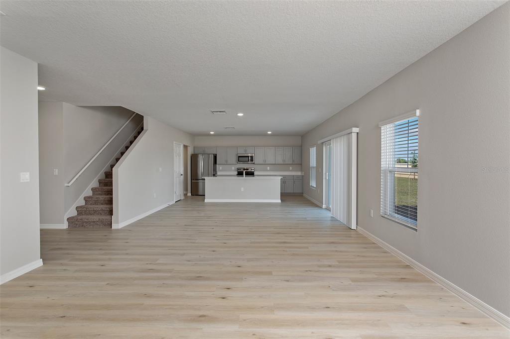 An open-concept kitchen and living area features light wood-look flooring and a carpeted staircase — 4361 RIVERBEND BOULEVARD, HAINES CITY, FL