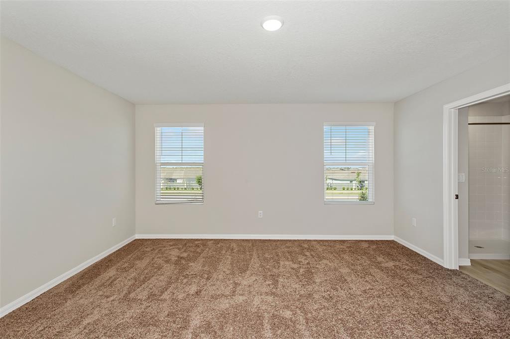 A carpeted bedroom features two windows and an adjacent bathroom with a shower — 4361 RIVERBEND BOULEVARD, HAINES CITY, FL