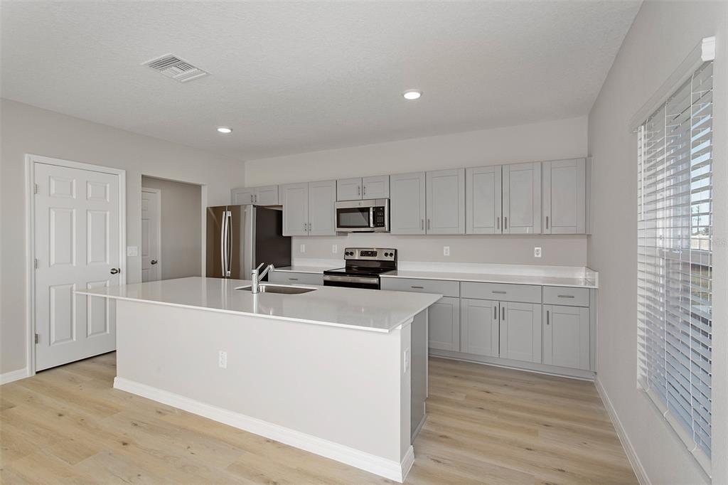 A modern kitchen features light gray cabinets, white countertops, a center island, and wood flooring — 4361 RIVERBEND BOULEVARD, HAINES CITY, FL