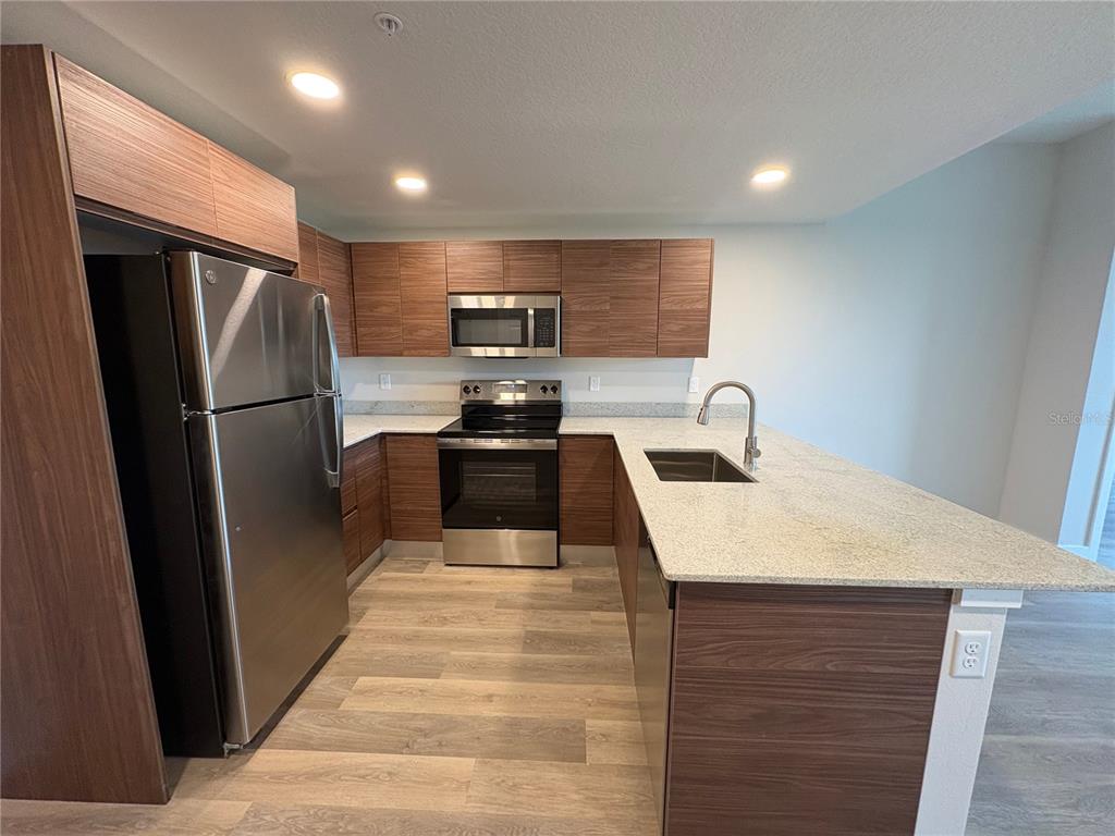 A kitchen features wood-grain cabinets, stainless steel appliances, and a granite-topped peninsula island — 4424 S TEXAS AVENUE UNIT 1-306, ORLANDO, FL