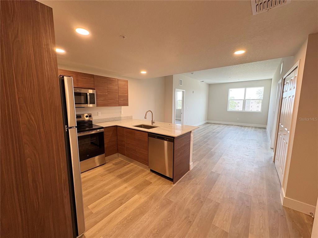A kitchen with wood-grain cabinets and stainless steel appliances opens into a living area — 4424 S TEXAS AVENUE UNIT 1-306, ORLANDO, FL