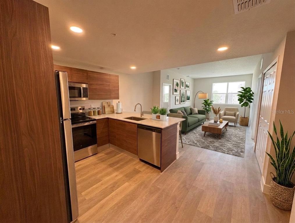 An open-concept kitchen with wood-grain cabinets and stainless steel appliances overlooks a furnished living area — 4424 S TEXAS AVENUE UNIT 1-306, ORLANDO, FL