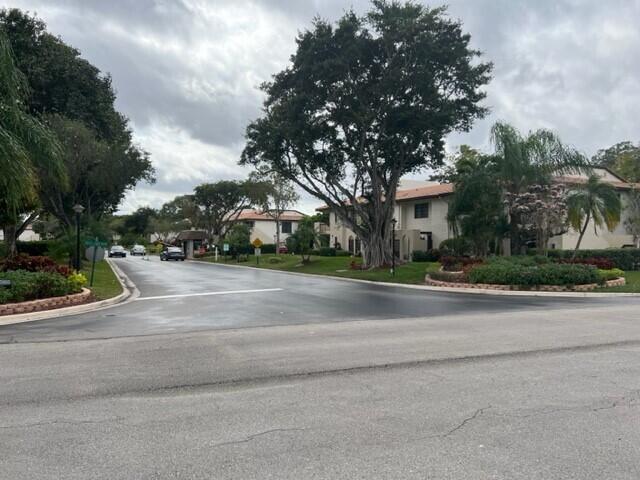 A paved road leads toward a gated entrance with multi-story buildings and large trees — 8436 Cypress Lane # 7d, Boca Raton FL 33433, BOCA RATON, FL