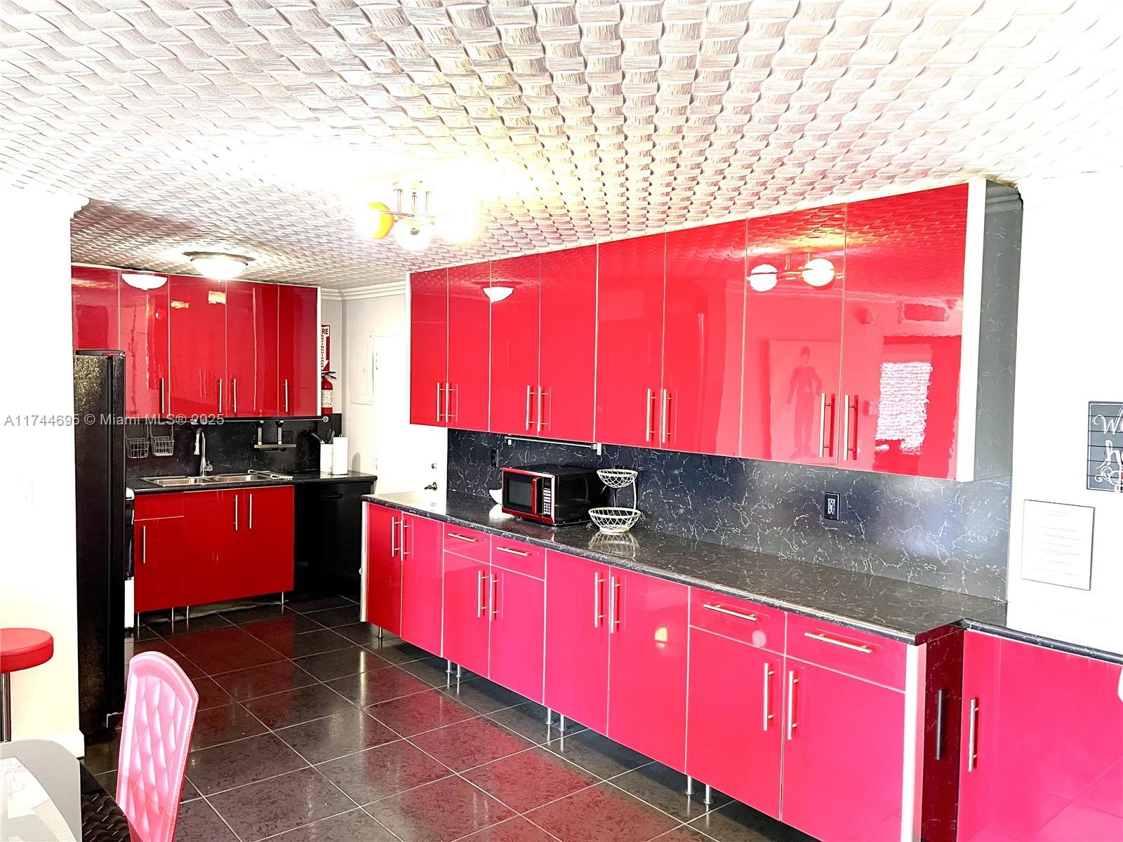 A kitchen features glossy red cabinets, black marble-patterned countertops, and a textured white ceiling — 200 178th Dr # 609, Sunny Isles Beach FL 33160, SUNNY ISLES BEACH, FL