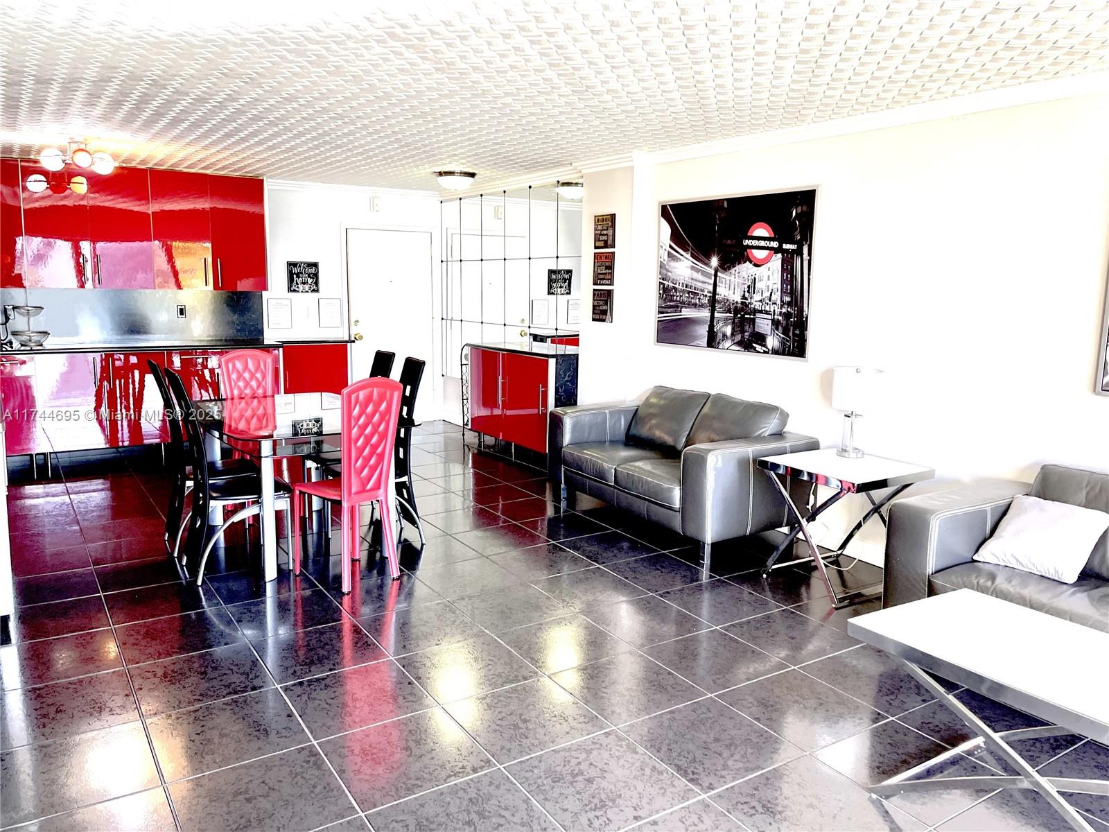 A living and dining area features red cabinets, dark tiled floors, and grey leather furniture — 200 178th Dr # 609, Sunny Isles Beach FL 33160, SUNNY ISLES BEACH, FL
