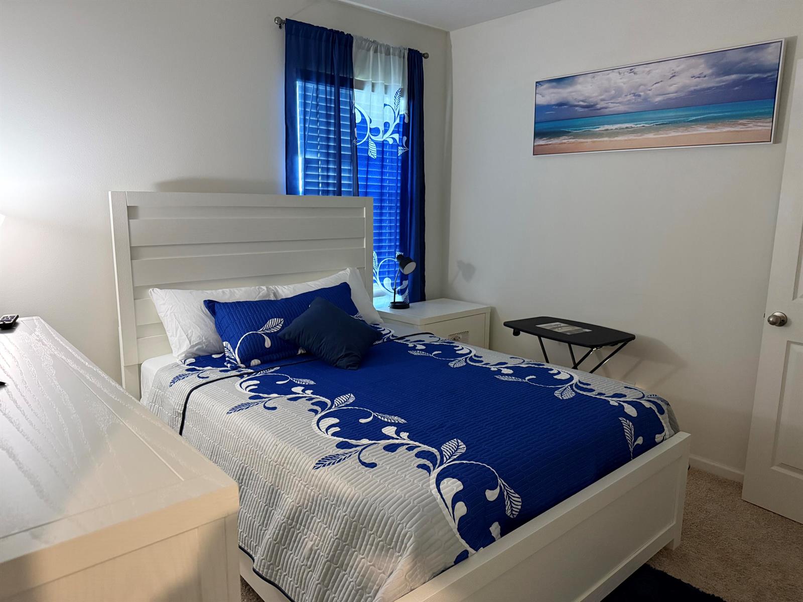 A bedroom features a white bed frame, blue and white bedding, and a beach wall art — 9511 Potomac Drive, Fort Pierce FL 34945, FORT PIERCE, FL
