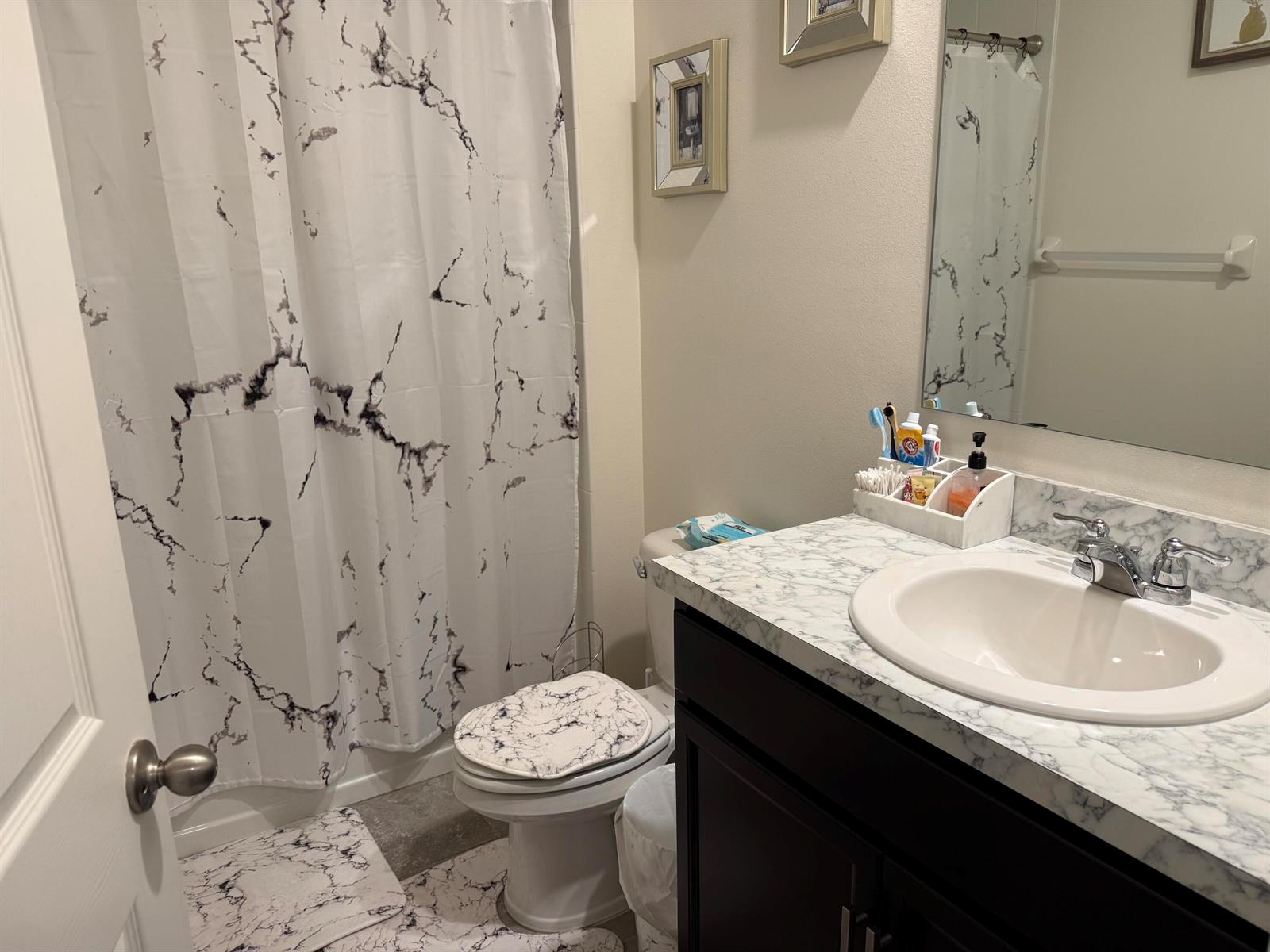 A bathroom features a marble-patterned shower curtain, toilet cover, and vanity countertop with dark cabinetry — 9511 Potomac Drive, Fort Pierce FL 34945, FORT PIERCE, FL