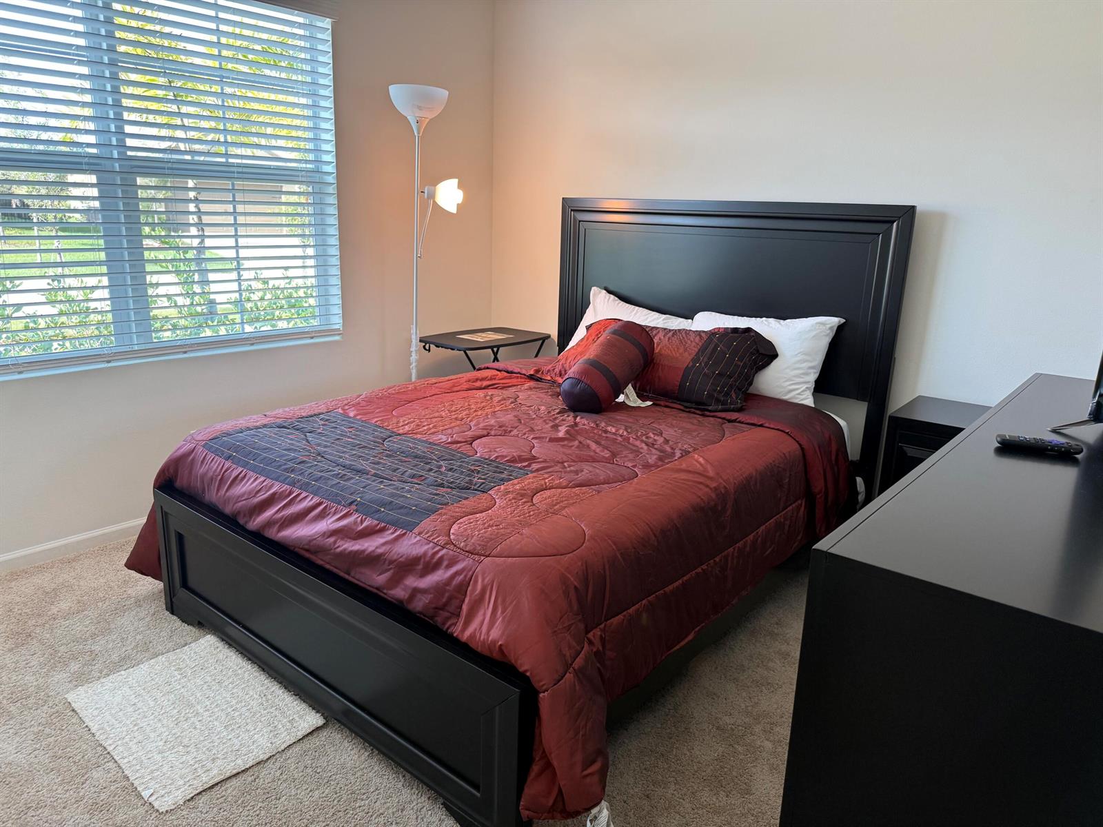 A bedroom features a black bed frame, a red patterned comforter, and a floor lamp — 9511 Potomac Drive, Fort Pierce FL 34945, FORT PIERCE, FL