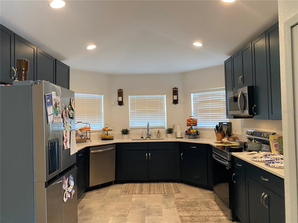 A kitchen features dark blue cabinets, stainless steel appliances, white countertops, and three windows — 1880 THOMPSON PRESERVE BOULEVARD, BARTOW, FL