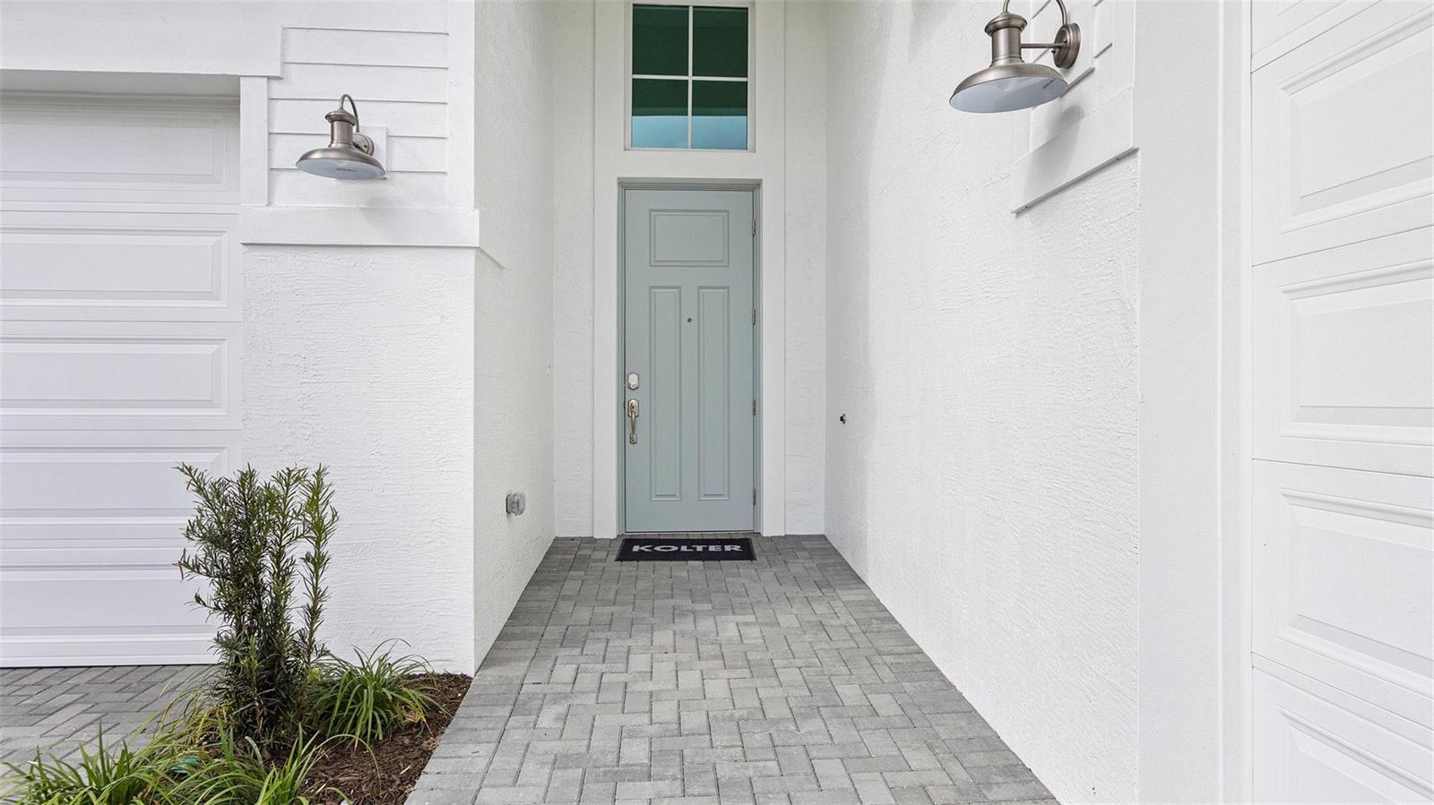 A light blue front door is centered between two garage doors on a paved entryway — 5237 Rivo Alto Circle, Westlake FL 33470, WESTLAKE, FL