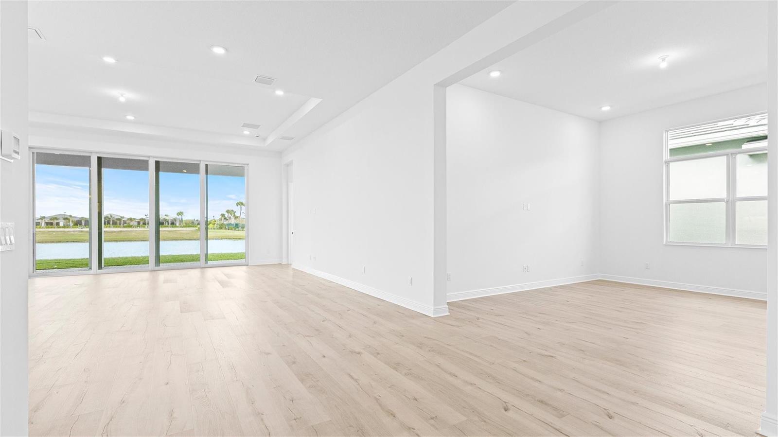 An open-concept living area features light wood flooring, white walls, and large sliding glass doors — 5237 Rivo Alto Circle, Westlake FL 33470, WESTLAKE, FL