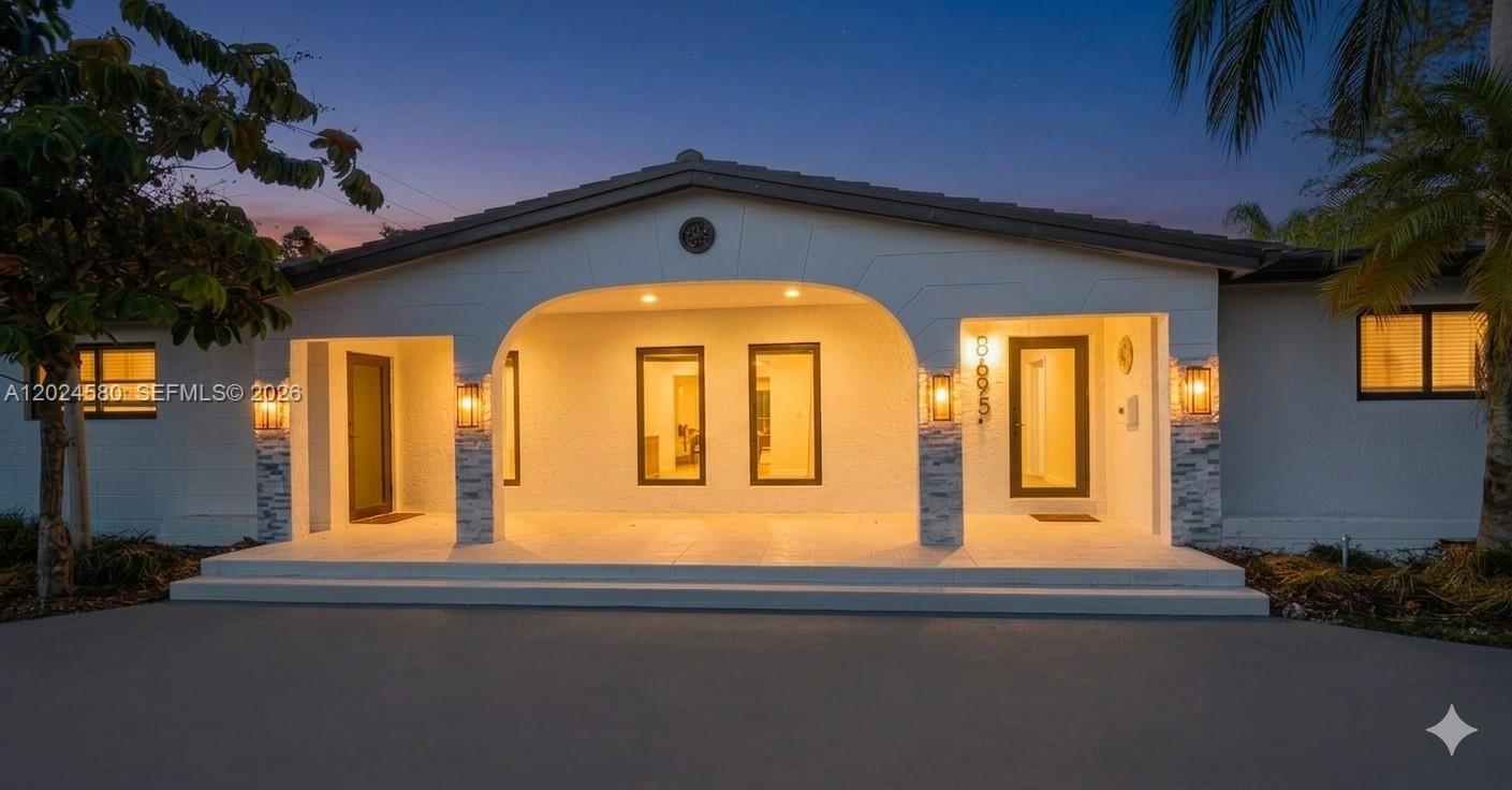 A white single-story house with a curved driveway and palm trees at dusk — 8695 SW 110th St, Miami FL 33156, MIAMI, FL