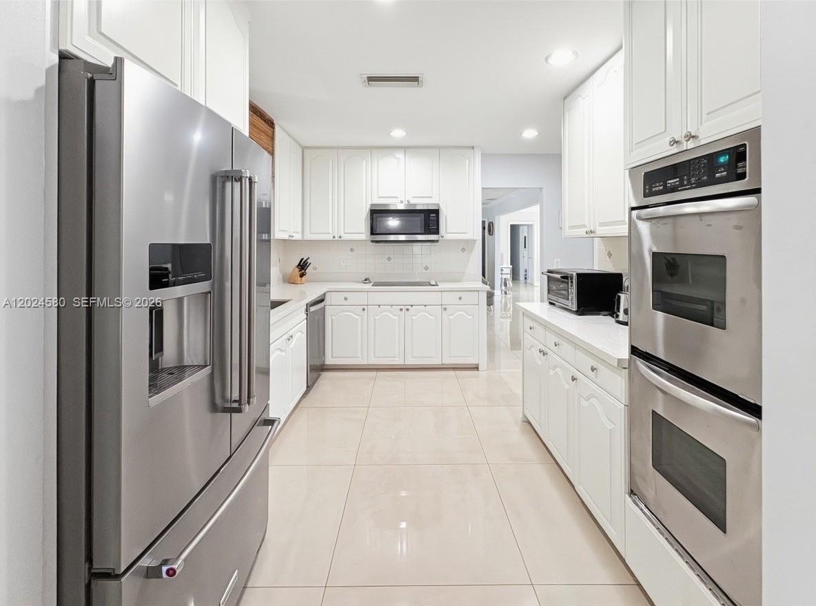 A galley-style kitchen features white cabinetry, stainless steel appliances, and light-colored tile flooring — 8695 SW 110th St, Miami FL 33156, MIAMI, FL