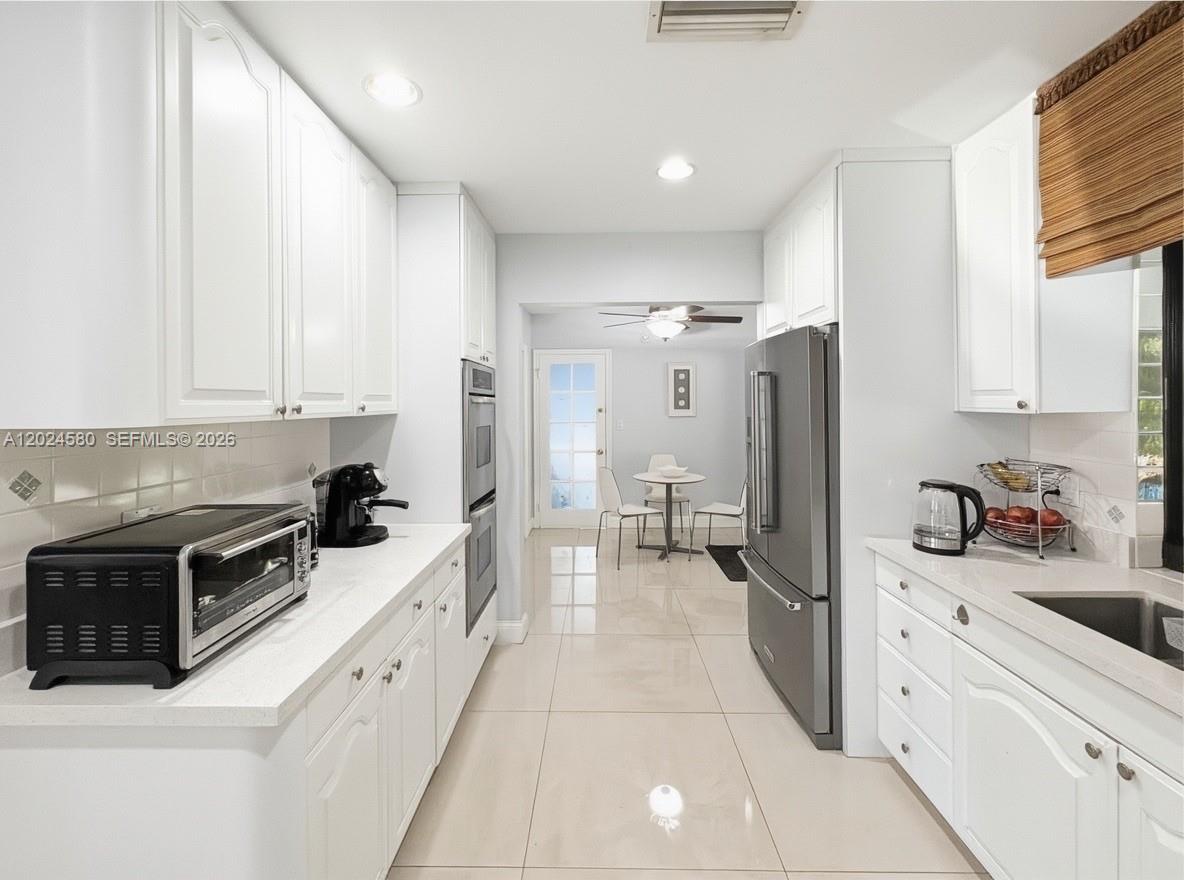 A galley kitchen features white cabinets, stainless steel appliances, and light-colored tile flooring — 8695 SW 110th St, Miami FL 33156, MIAMI, FL