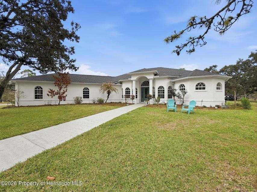 A white, single-story house with a dark roof and arched windows sits on a lawn — 12124 SQUEEZE AVENUE, BROOKSVILLE, FL