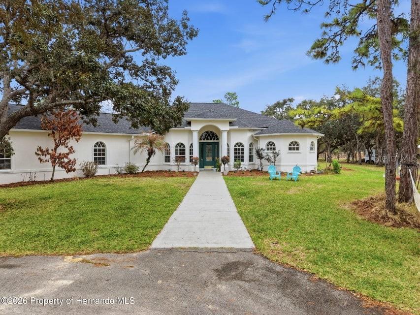 A single-story white house with a dark roof and a central arched entryway — 12124 SQUEEZE AVENUE, BROOKSVILLE, FL