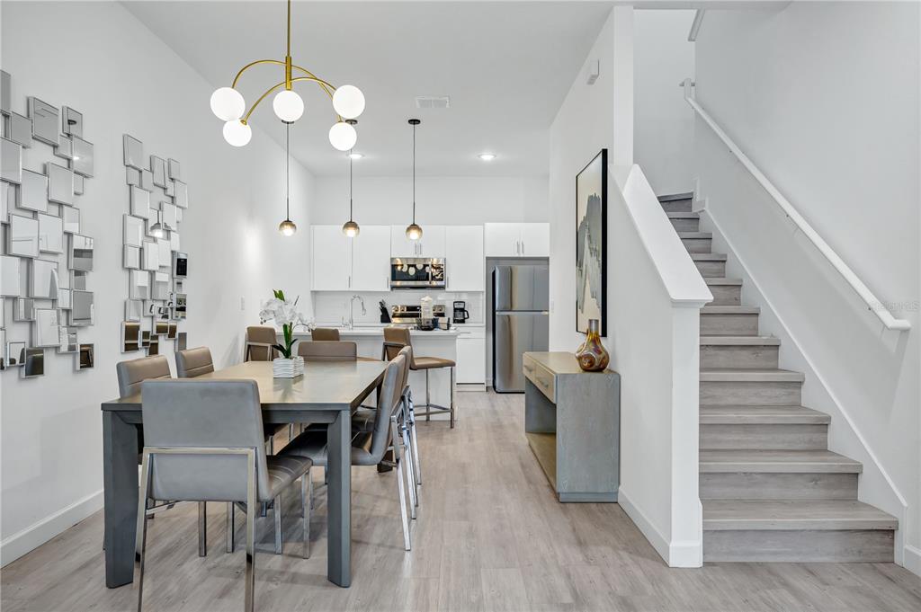 A modern dining area and kitchen feature light wood flooring, white cabinetry, and a staircase — 513 FAMAGUSTA DRIVE, DAVENPORT, FL