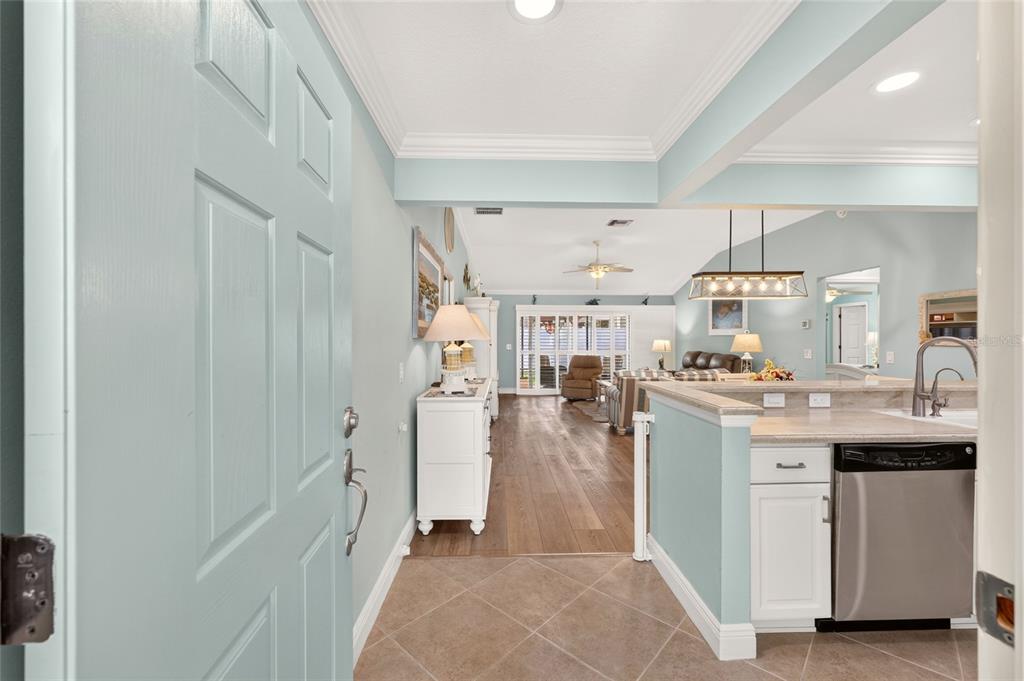A view from an entryway into a kitchen and living area with light blue walls — 1613 PENNECAMP DRIVE, THE VILLAGES, FL