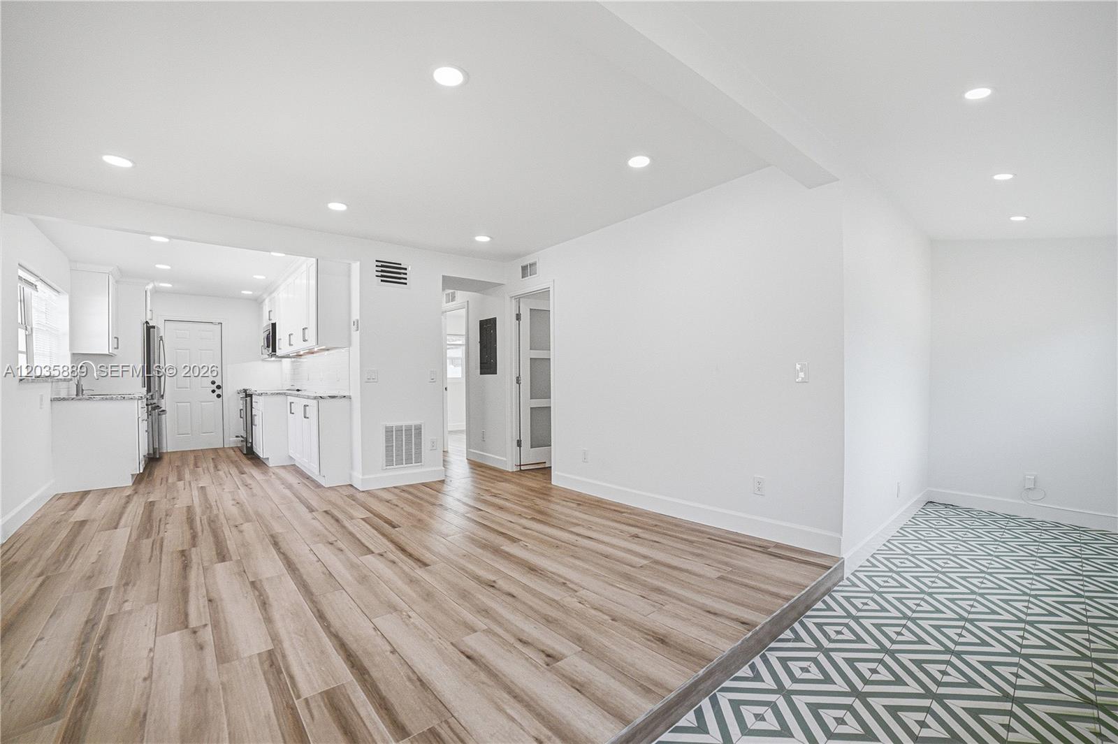 A bright, open-concept room features wood-look flooring, white walls, and an adjacent white kitchen — 335 NE 12th Ave, Boynton Beach FL 33435, BOYNTON BEACH, FL