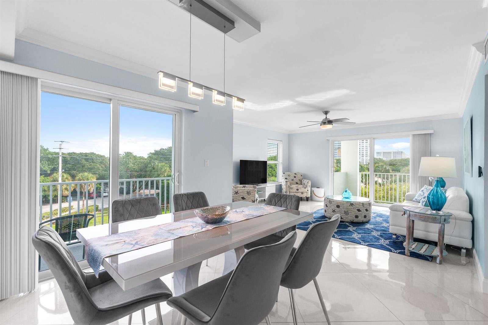A bright, open-concept living and dining area features light blue walls, tile floors, and balconies — 950 Ponce De Leon Road # 401, Boca Raton FL 33432, BOCA RATON, FL