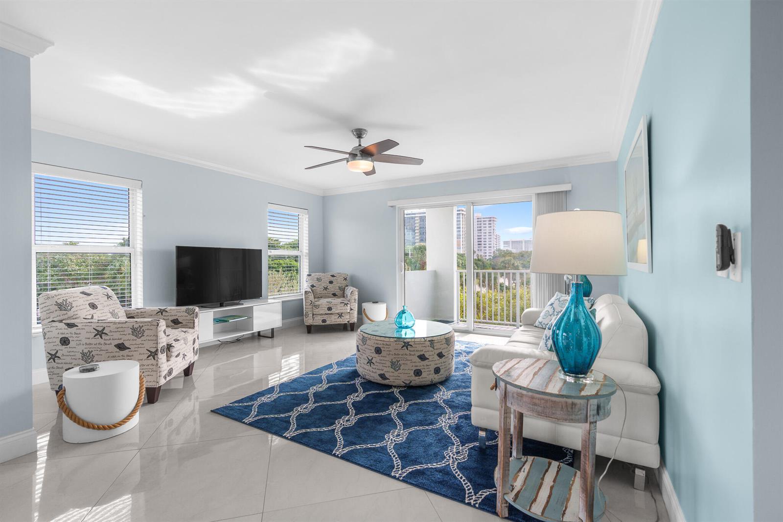 A bright living room features light blue walls, tile floors, a blue rug, and balcony views — 950 Ponce De Leon Road # 401, Boca Raton FL 33432, BOCA RATON, FL