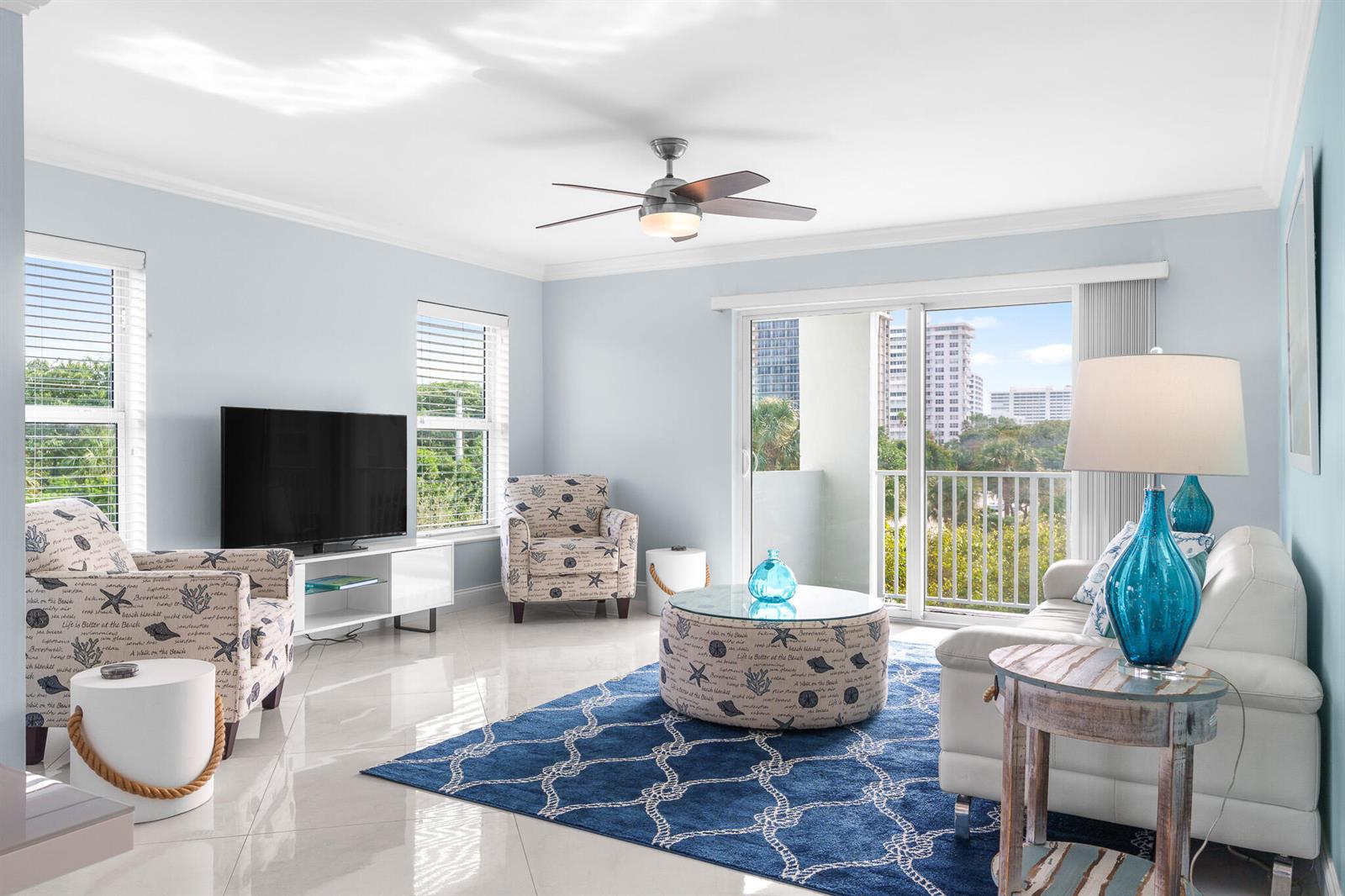 A bright living room features a blue patterned rug, white sofa, armchairs, and balcony views — 950 Ponce De Leon Road # 401, Boca Raton FL 33432, BOCA RATON, FL