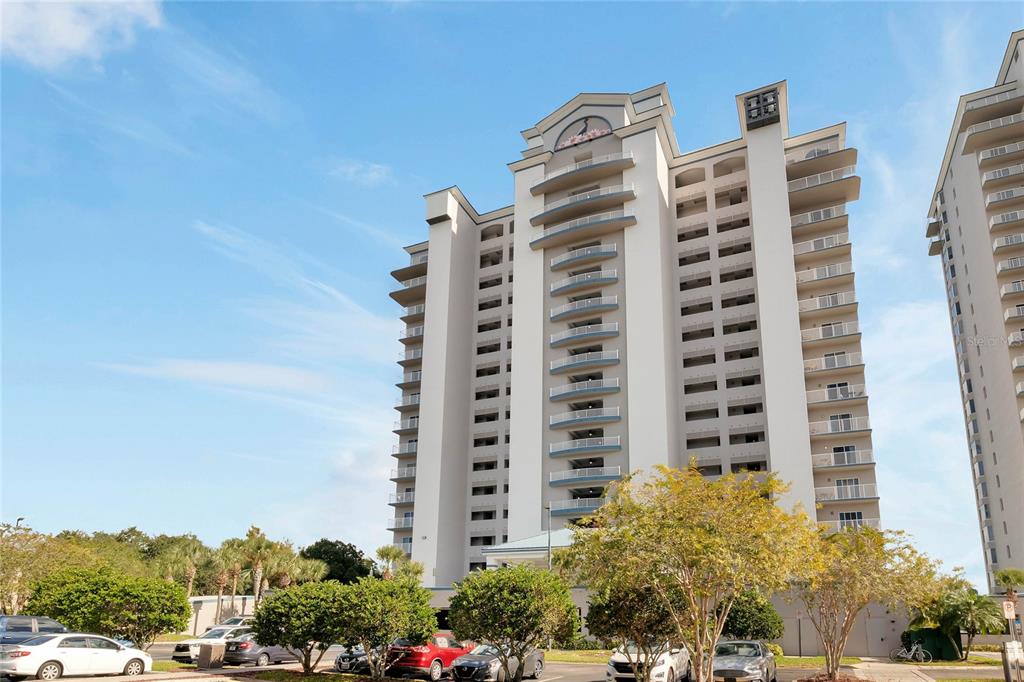 A tall, white multi-story residential building with numerous balconies stands under a blue sky — 13415 BLUE HERON BEACH DRIVE UNIT 606, ORLANDO, FL