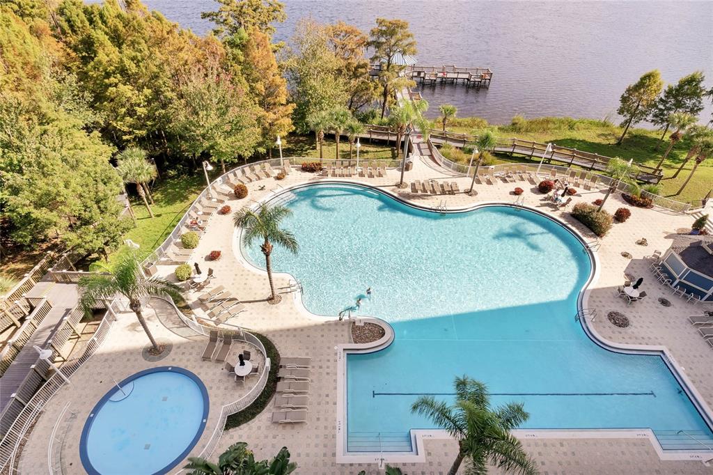 An aerial view shows a large swimming pool and a smaller circular pool by a lake — 13415 BLUE HERON BEACH DRIVE UNIT 606, ORLANDO, FL