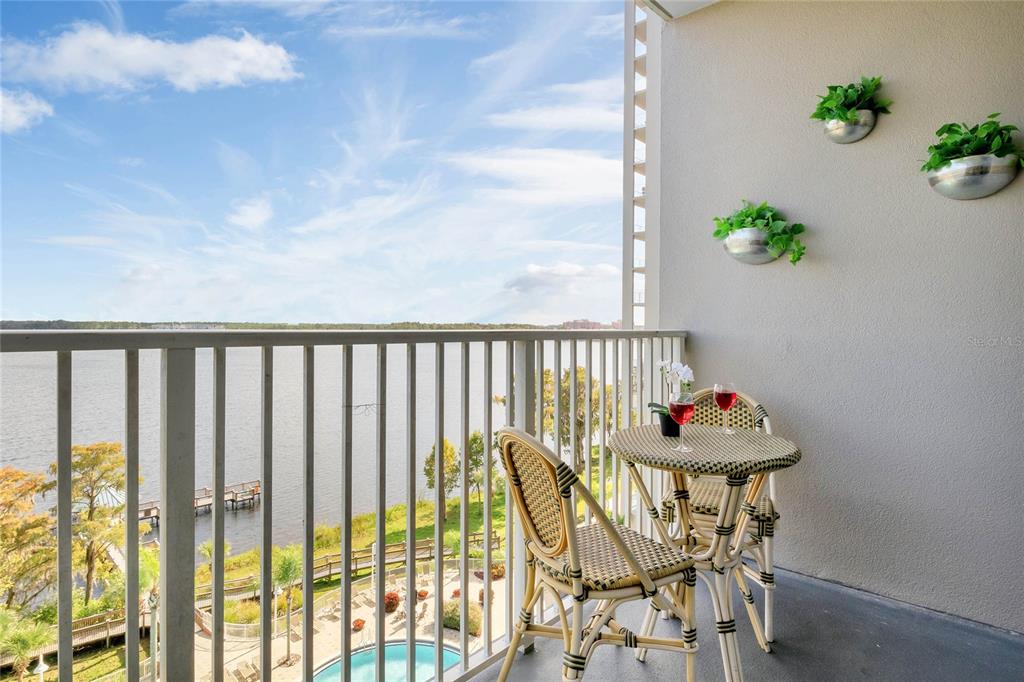 A balcony features a small bistro set, wall-mounted planters, and a view of a lake — 13415 BLUE HERON BEACH DRIVE UNIT 606, ORLANDO, FL