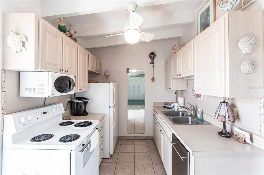 A galley-style kitchen features white cabinets, light countertops, a white stove, and a ceiling fan — 6006 MIDNIGHT PASS ROAD UNIT 68, SARASOTA, FL