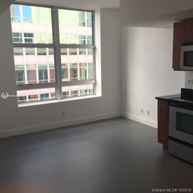A kitchen area with stainless steel appliances and large windows overlooking a neighboring building — 111 E Flagler St # 1003, Miami FL 33131, MIAMI, FL