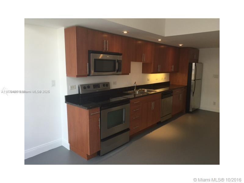 A kitchen features wood cabinets, black countertops, stainless steel appliances, and gray flooring — 111 E Flagler St # 1003, Miami FL 33131, MIAMI, FL