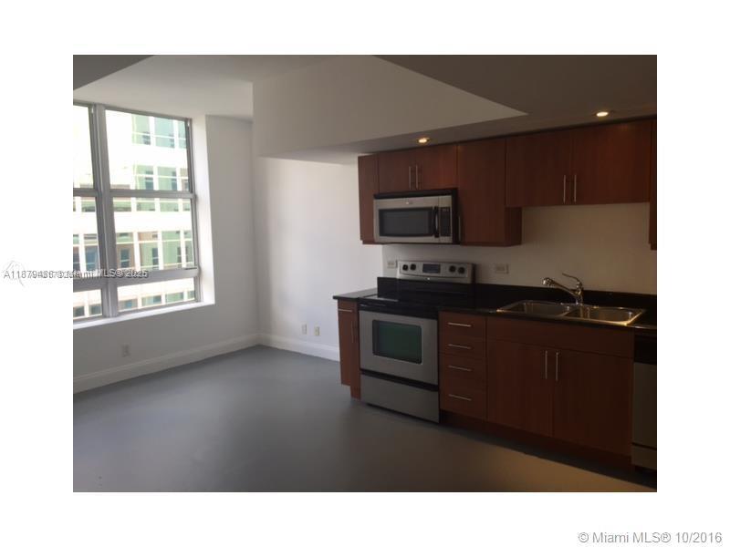 A kitchen with wood cabinets and stainless steel appliances sits next to a large window — 111 E Flagler St # 1003, Miami FL 33131, MIAMI, FL