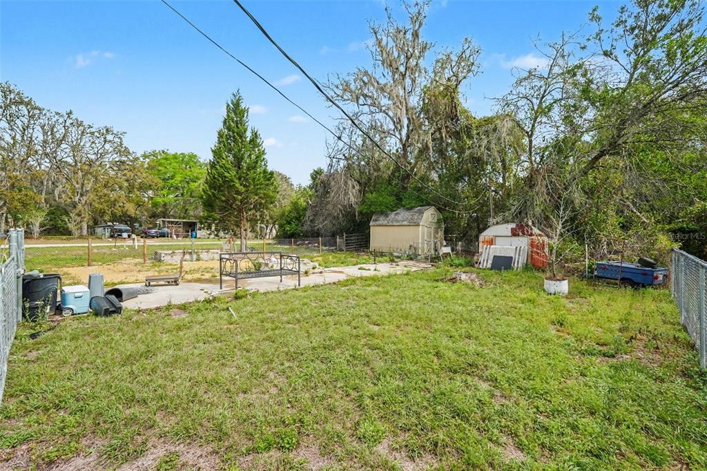 A grassy backyard features a concrete patio, a metal bench, and two small storage sheds — 34884 REYNOLDS STREET, DADE CITY, FL