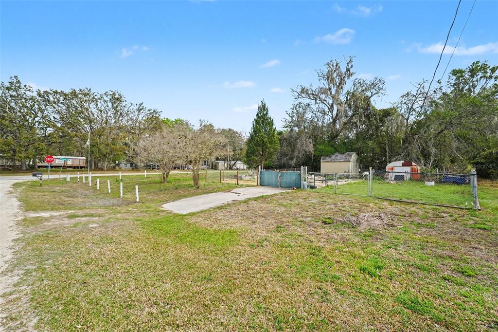 A grassy lot features a concrete driveway, a chain-link fence, and a small storage shed — 34884 REYNOLDS STREET, DADE CITY, FL
