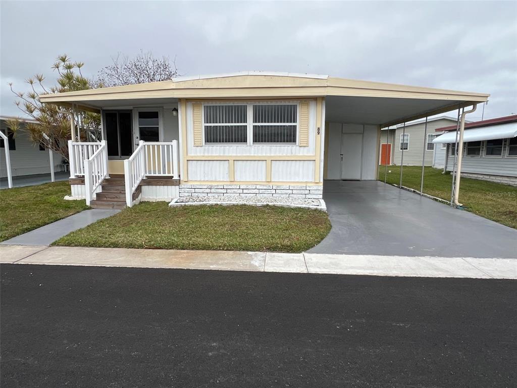 A single-story manufactured home features a front porch, a carport, and a paved driveway — 11300 124TH AVENUE UNIT 89, LARGO, FL