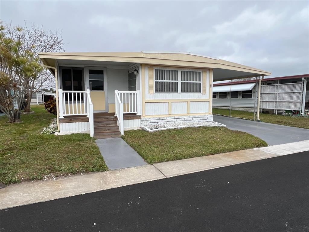 A single-story mobile home with a front porch, carport, and light-colored siding — 11300 124TH AVENUE UNIT 89, LARGO, FL