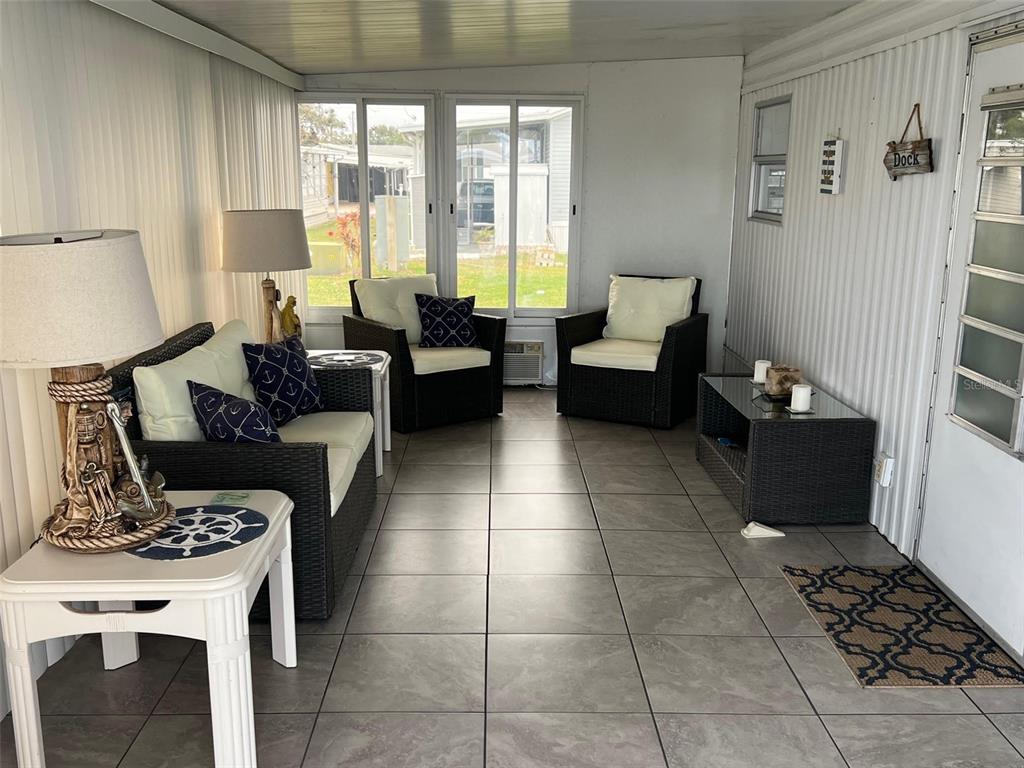 A sunroom features tiled floors, wicker furniture with white cushions, and large windows — 11300 124TH AVENUE UNIT 89, LARGO, FL