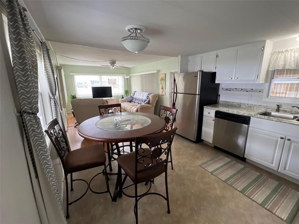An open-concept kitchen and dining area features a round table, stainless appliances, and white cabinets — 11300 124TH AVENUE UNIT 89, LARGO, FL