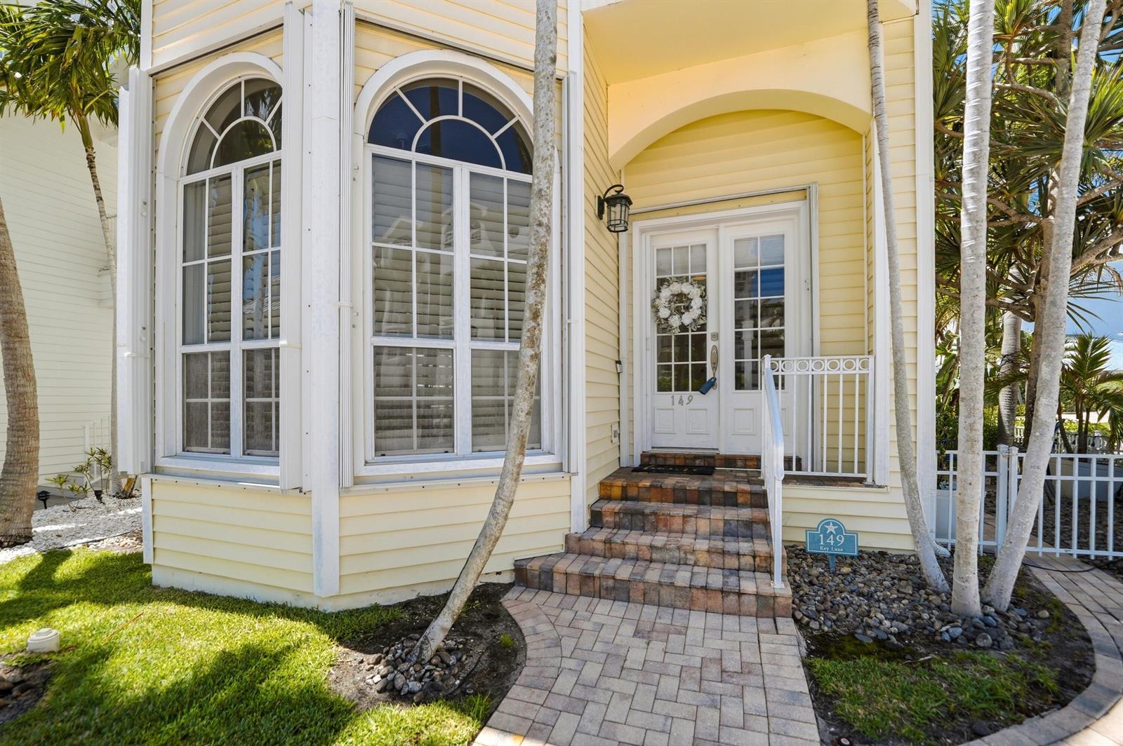A yellow house exterior features a brick walkway, arched windows, and a double front door — 149 Key Lane, Jupiter FL 33477, JUPITER, FL