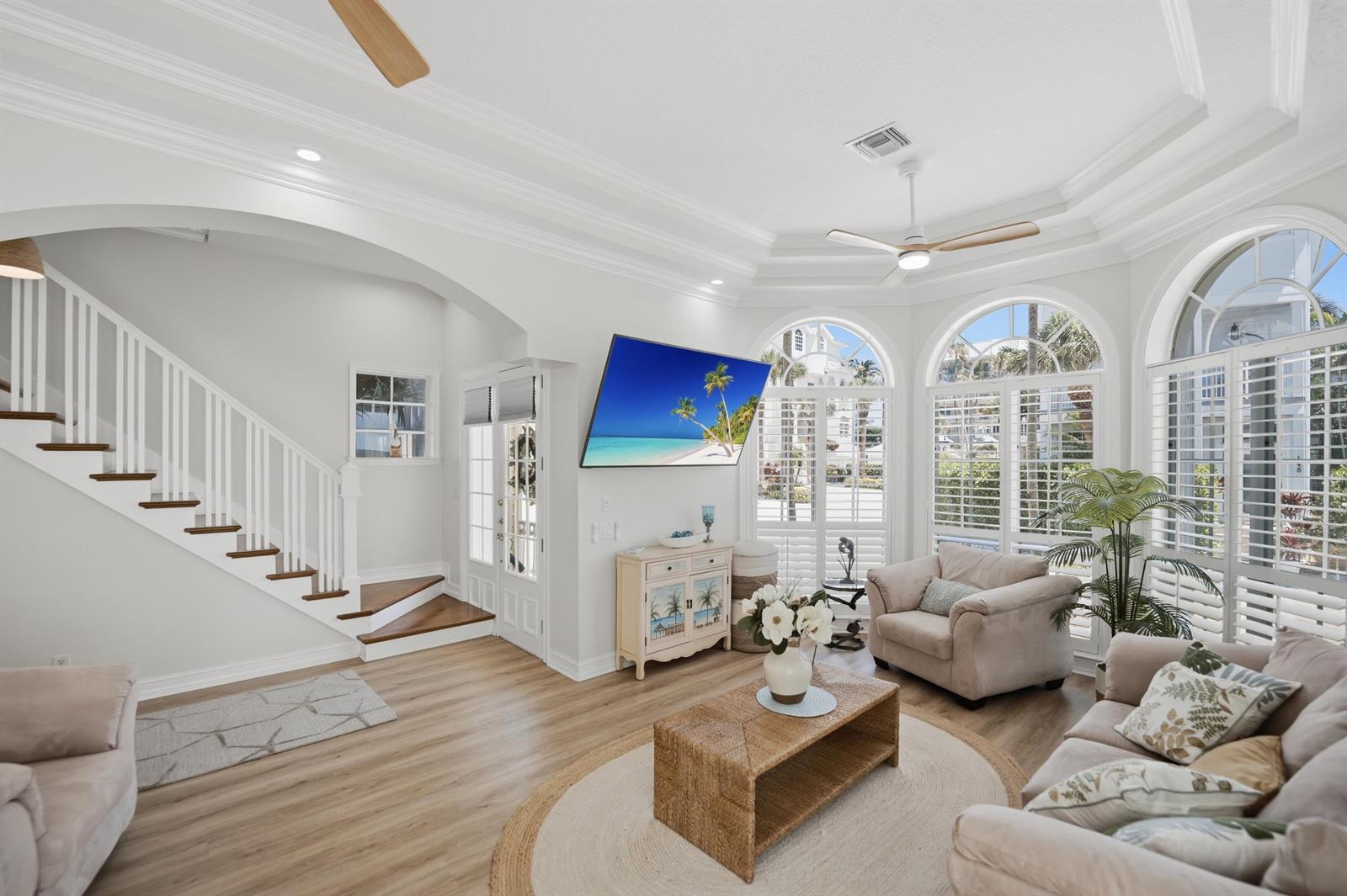 A bright living room features a staircase, arched windows with shutters, and a wall-mounted television — 149 Key Lane, Jupiter FL 33477, JUPITER, FL