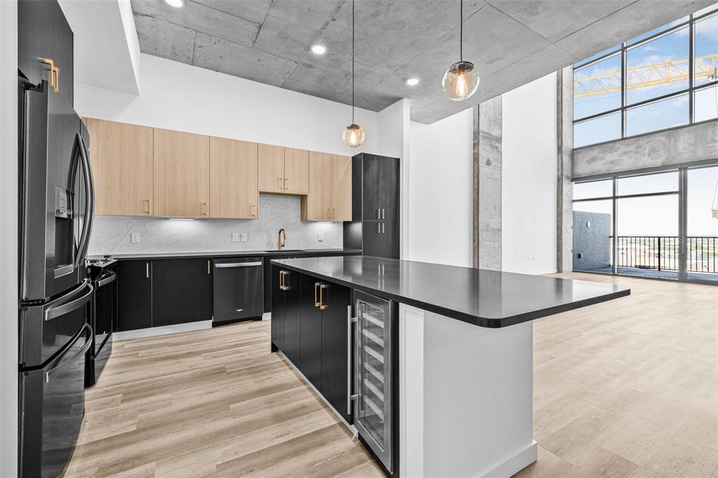 A modern kitchen features two-tone cabinetry, a black island with a wine cooler, and concrete ceilings — 221 MAIN STREET N UNIT PH 1603, ST PETERSBURG, FL