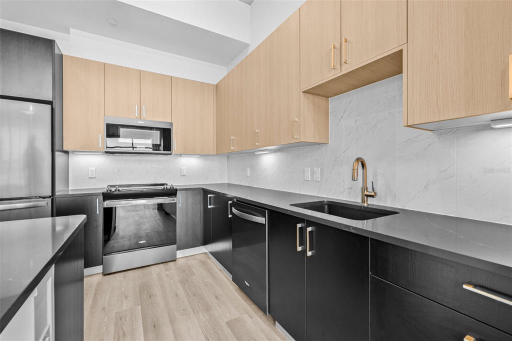 A modern kitchen features two-toned cabinetry, stainless steel appliances, and a marble-patterned backsplash — 221 MAIN STREET N UNIT PH 1603, ST PETERSBURG, FL