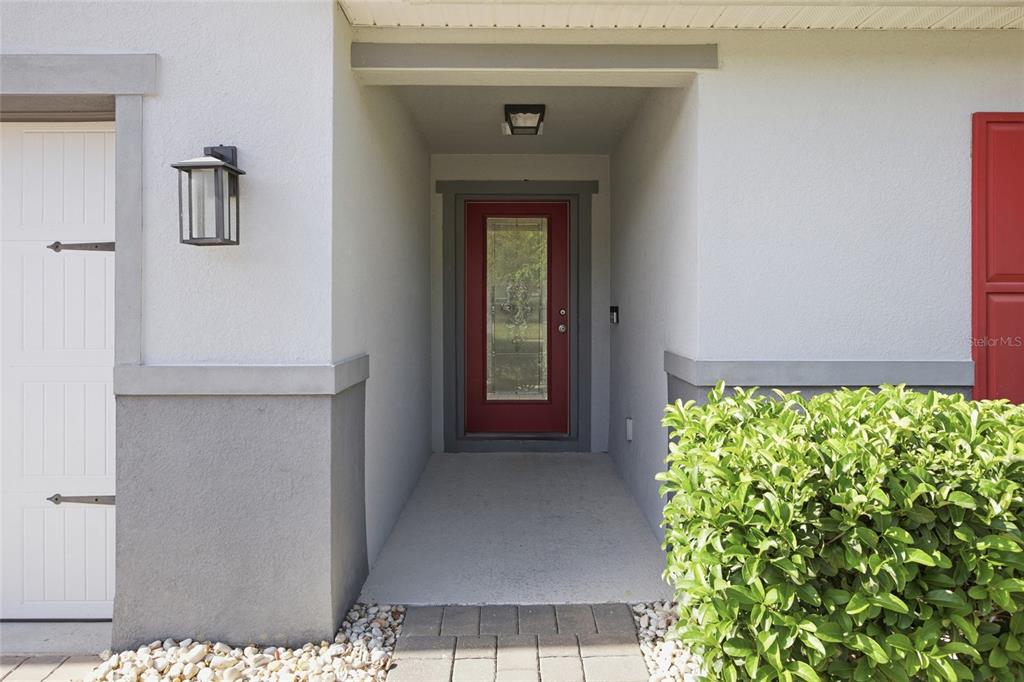 A red front door is centered in a covered entryway with gray stucco walls — 6461 DOMENICO COURT, GROVELAND, FL