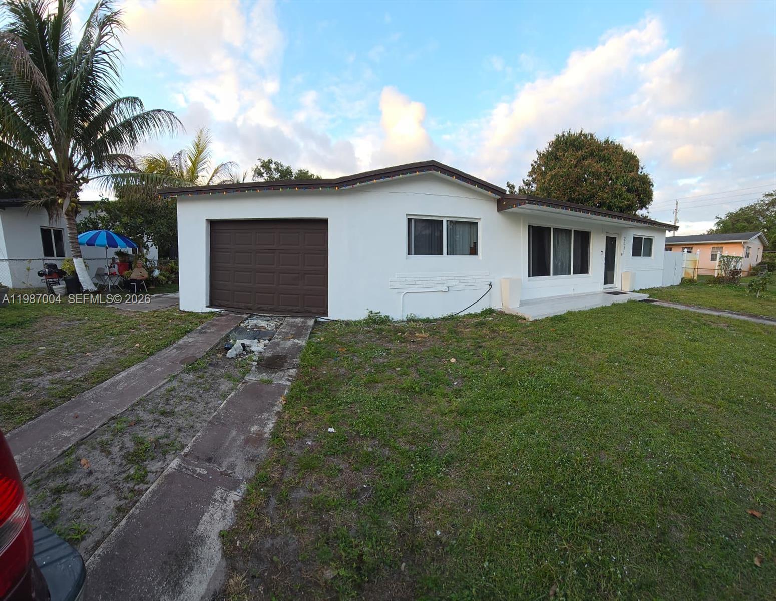 A white single-story house features a brown garage door and a front lawn — 2011 NW 178th St, Miami Gardens FL 33056, MIAMI GARDENS, FL