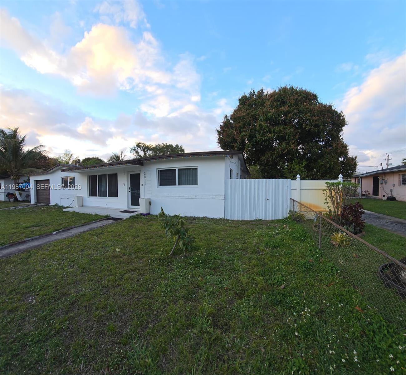 A white single-story house features a front lawn, a driveway, and a white privacy fence — 2011 NW 178th St, Miami Gardens FL 33056, MIAMI GARDENS, FL